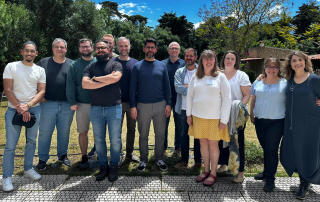 grupo de 14 pessoas posando ao ar livre em um dia ensolarado, com árvores ao fundo