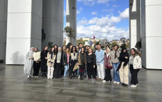 Grupo de pessoas posando em frente a um edifício e sorrindo.